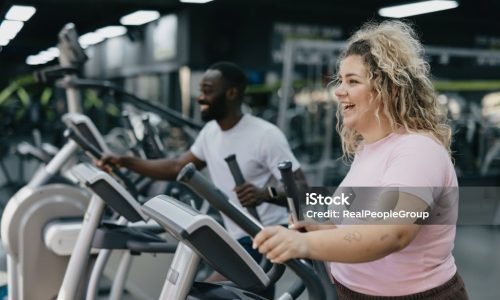 cardio A vibrant fitness atmosphere with a woman and her trainer working out on elliptical machines, representing dedication to health and the collaboration between trainer and trainee.