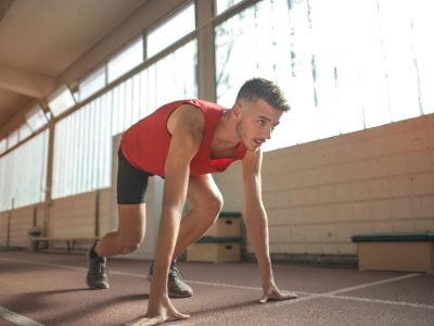 Focused male athlete in starting position indoors, ready to sprint.
