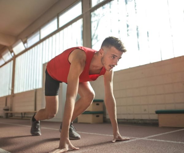 Focused male athlete in starting position indoors, ready to sprint.